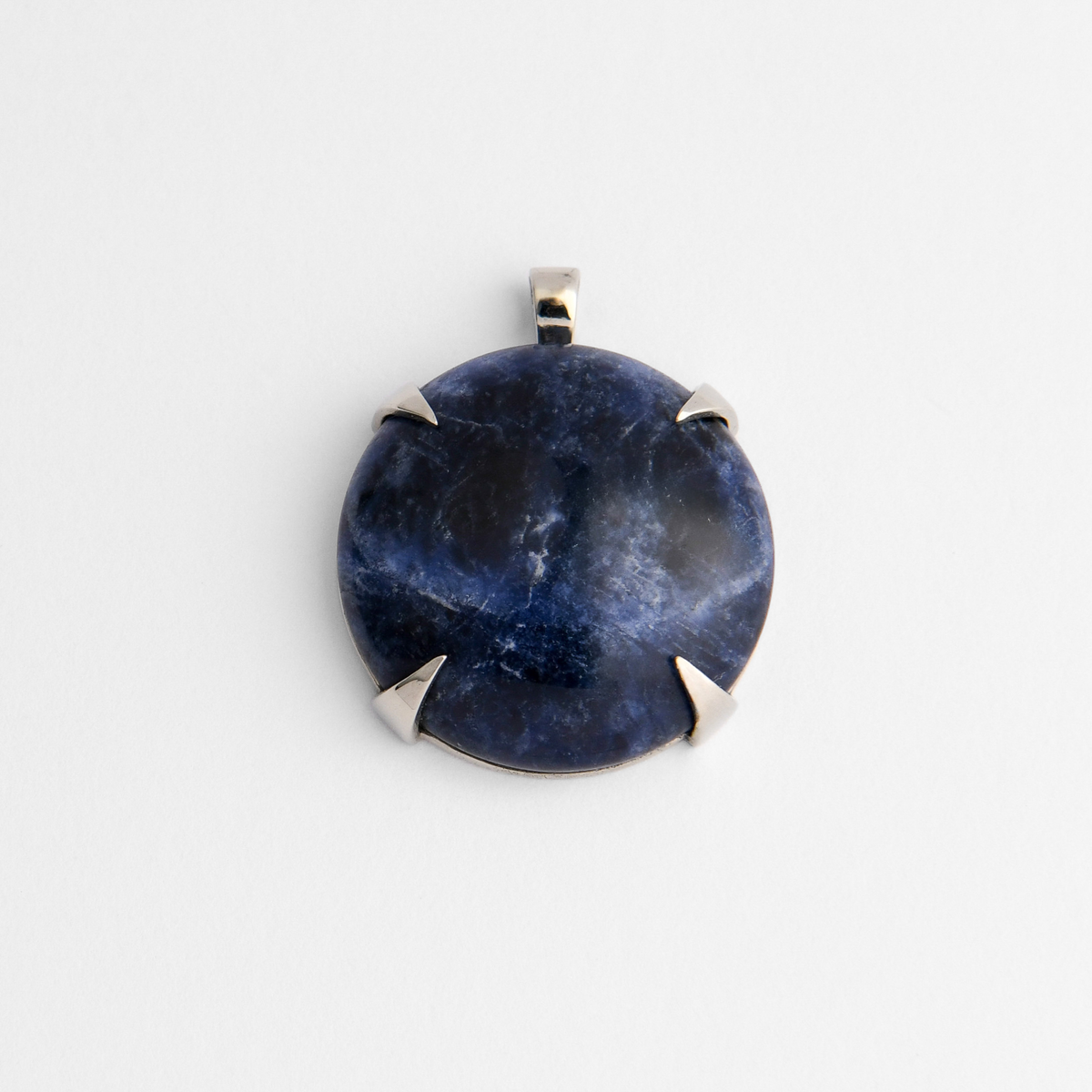 Spar, a round pendant in cool, silvery white bronze, with four triangular claws holding blue sodalite, ranging from deep midnight to brighter blue, with irregular white veining and occasional biscuit-coloured markings. As a natural stone, each piece varies.