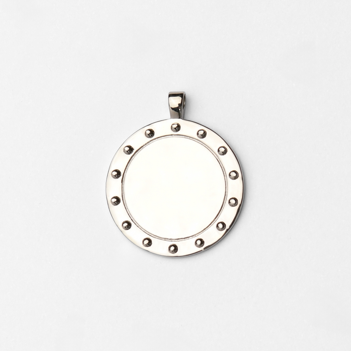 Horo, a round pendant in cool, silvery white bronze, with a smooth circular centre bordered by a ring of small raised studs.