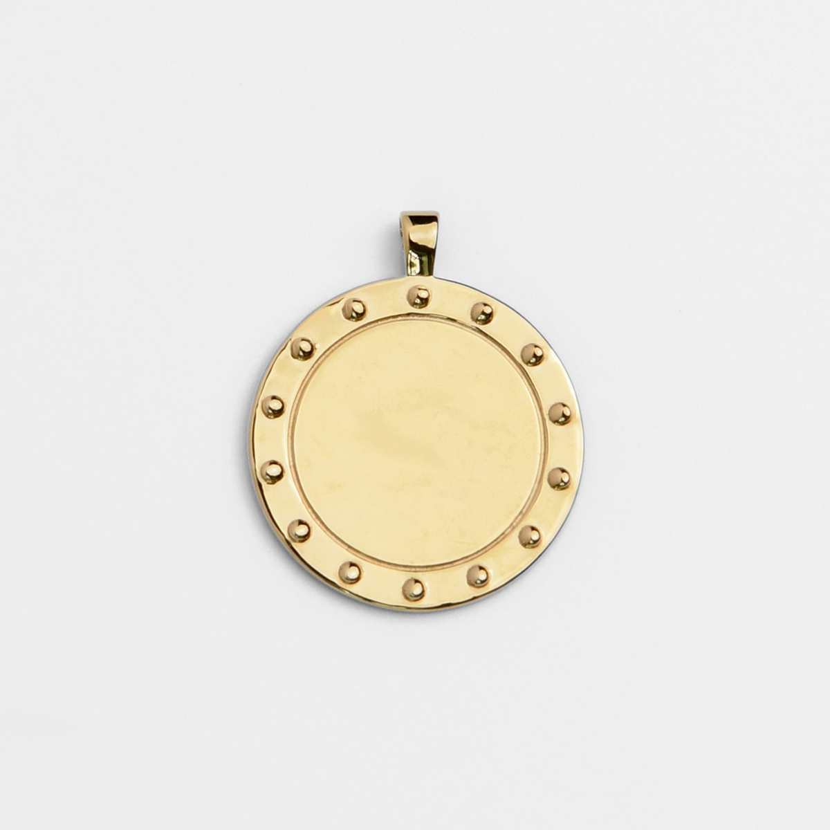Horo, a round pendant in warm, golden-yellow brass, with a smooth circular centre bordered by a ring of small raised studs.