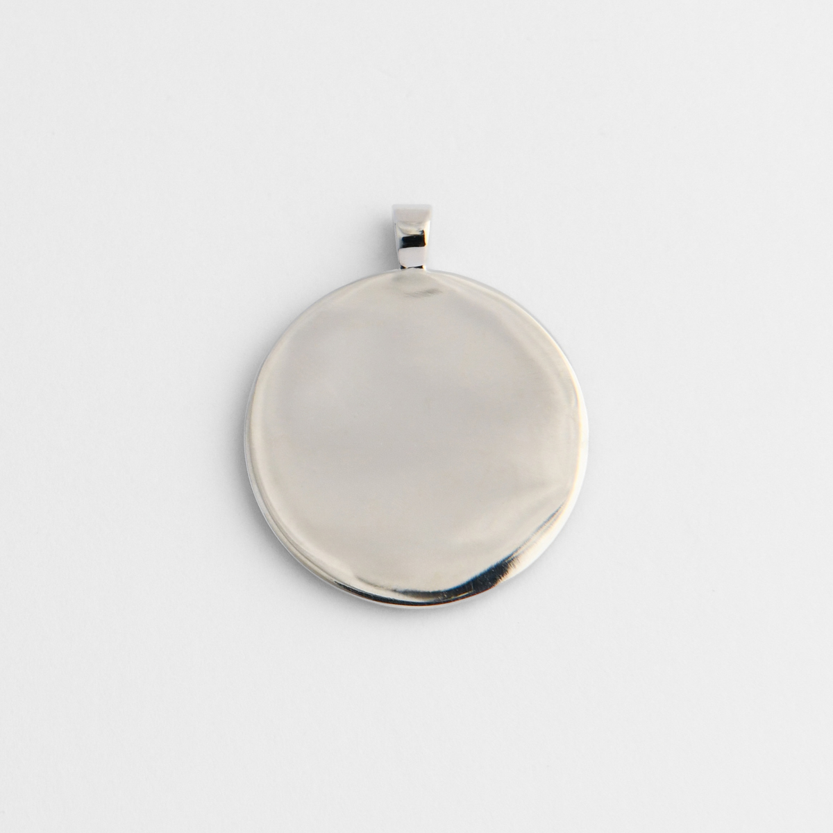 Back of Horo, a round pendant in cool, silvery white bronze, showing its smooth, flat reverse for personalised engraving.