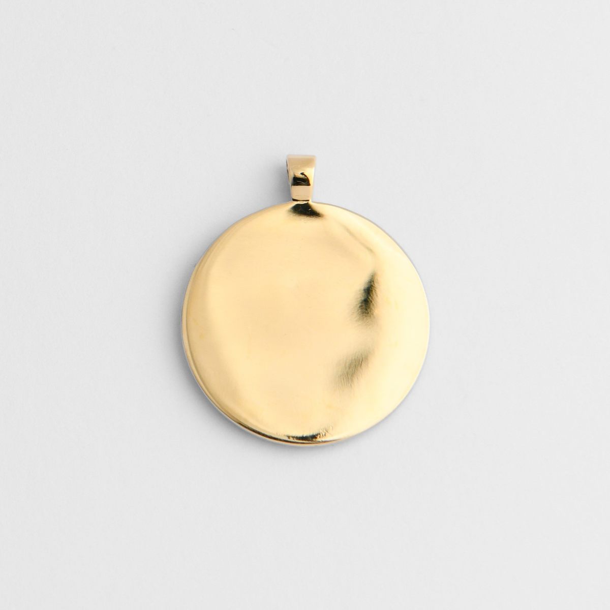 Back of Horo, a round pendant in warm, golden-yellow brass, showing its smooth, flat reverse for personalised engraving.
