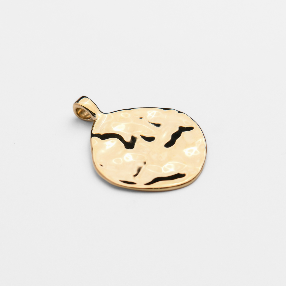 Vea, an irregularly rounded pendant in warm, golden-yellow brass, with a hammered surface creating an uneven, dappled pattern of light and shadow.