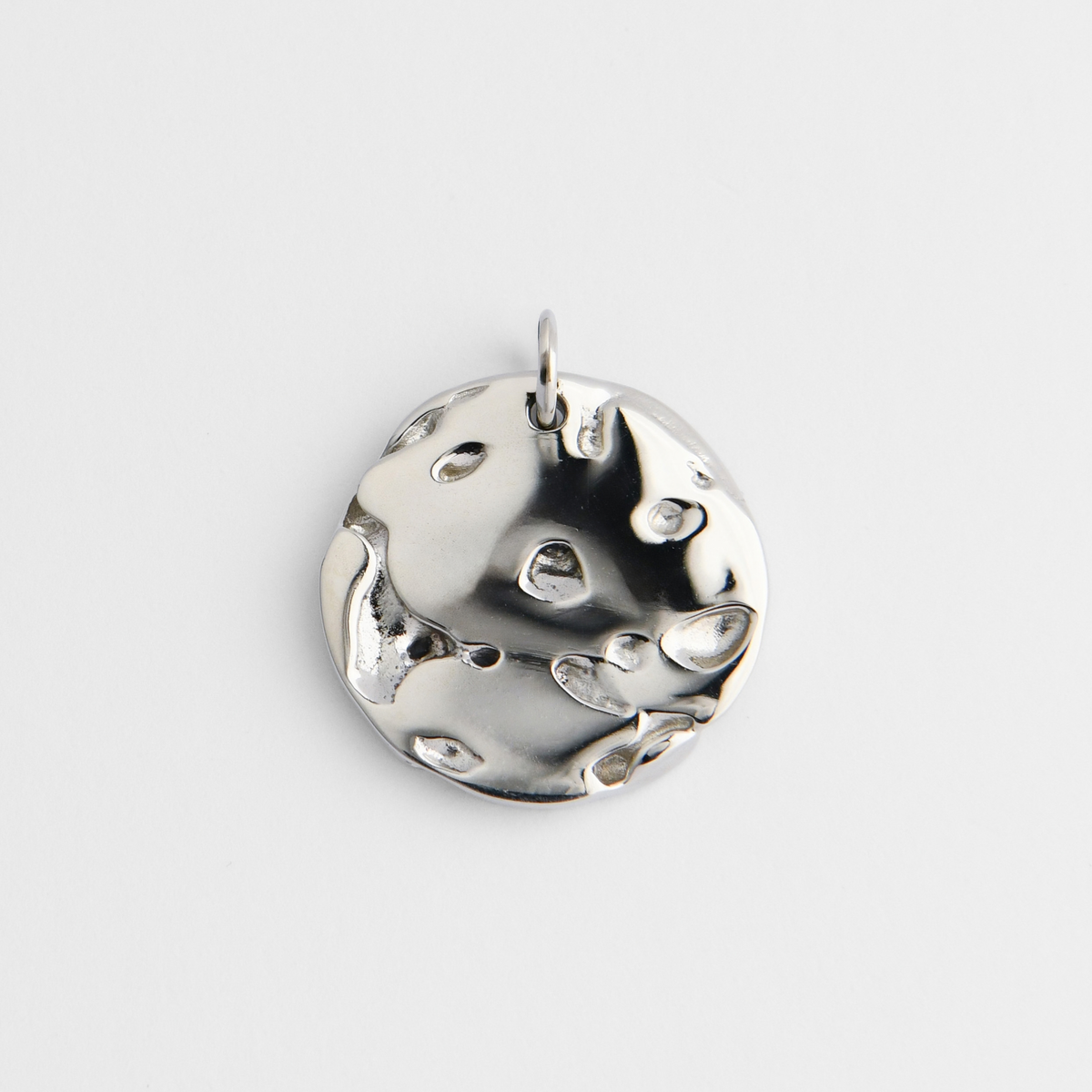 Bolide, a round pendant in cool, silvery white bronze, with an irregular, cratered surface of smooth hollows and raised molten-like forms.