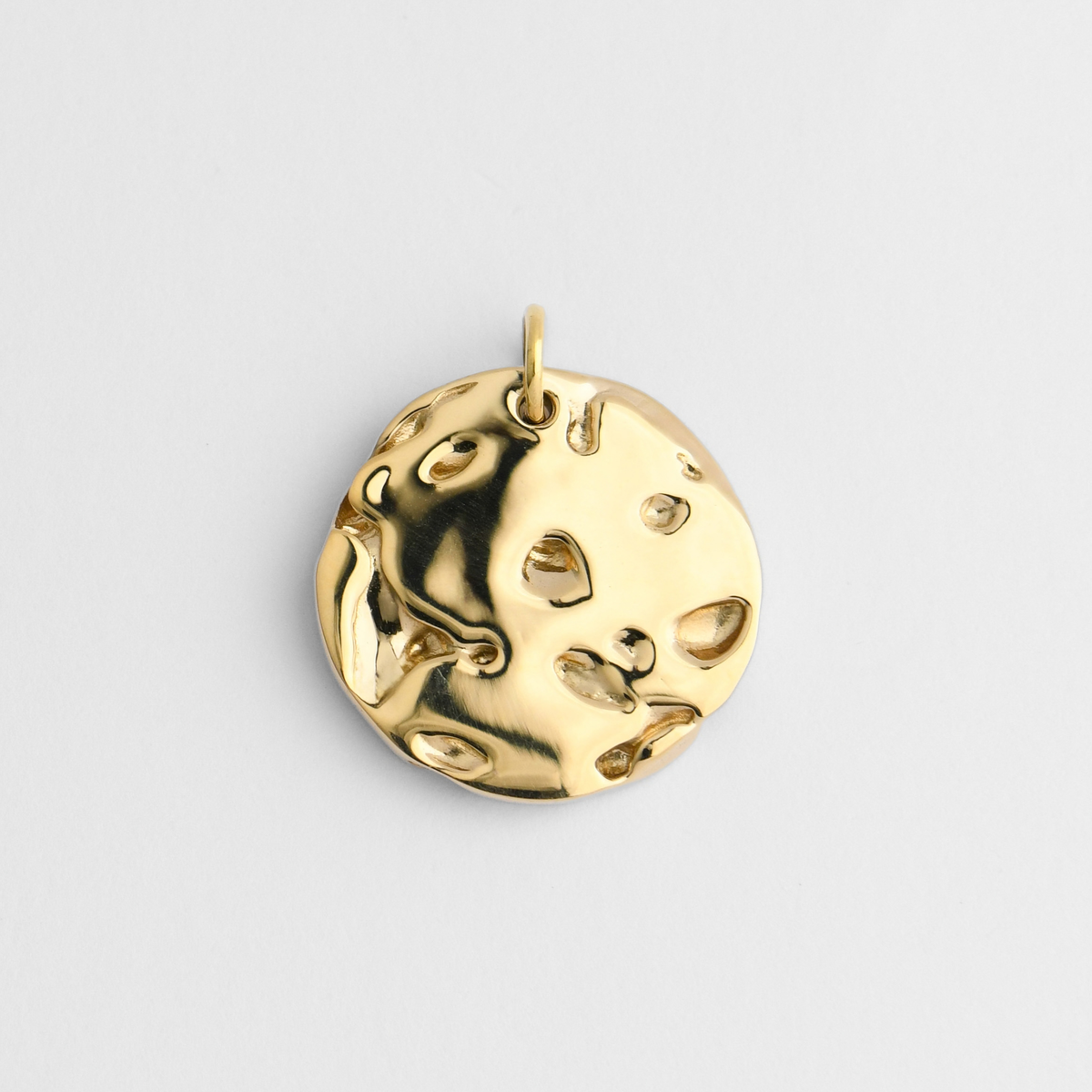 Bolide, a round pendant in warm, golden-yellow brass, with an irregular, cratered surface of smooth hollows and raised molten-like forms.