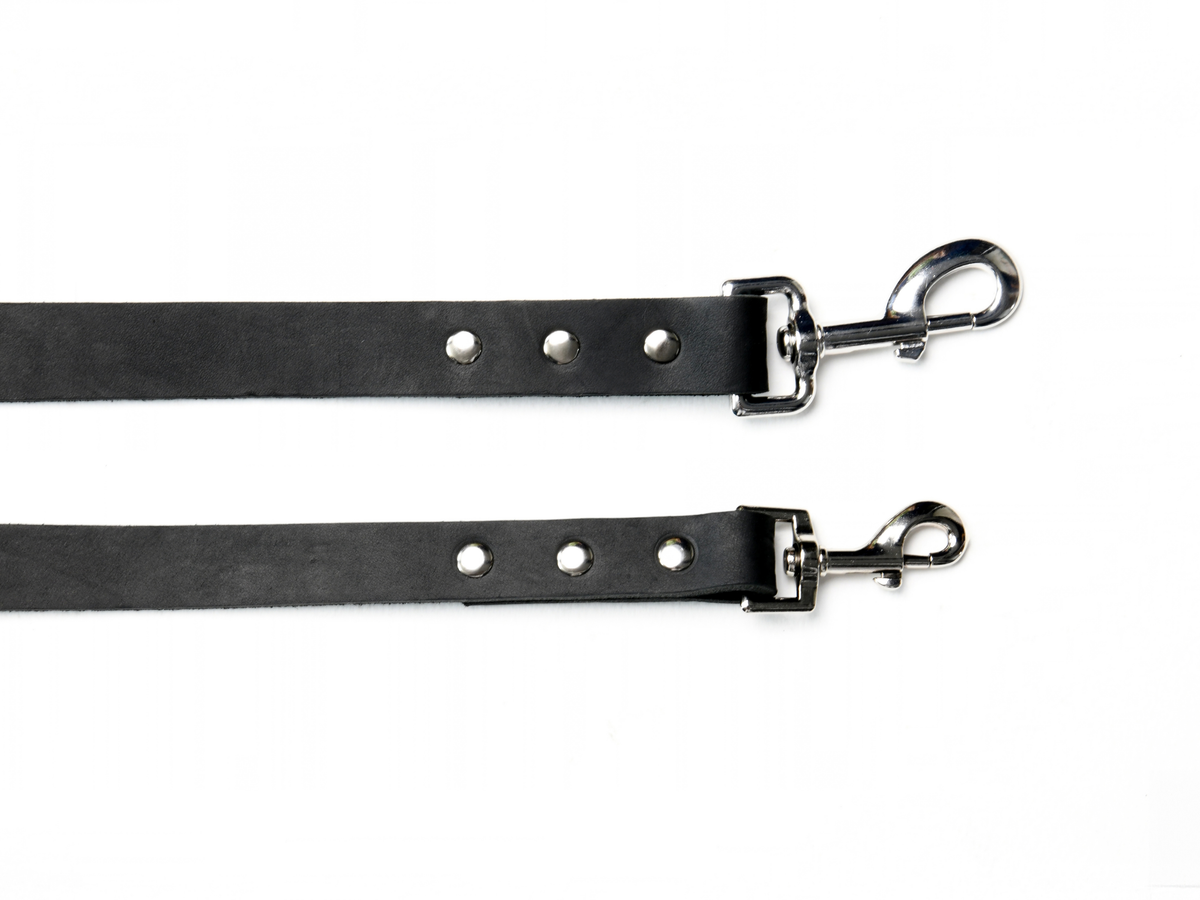 Two black cowhide leather dog leads in XS/S and M/L sizes, shown together to compare their widths and sizes of the silver-colour zinc alloy trigger clips. Each clip is secured with three metal studs.
