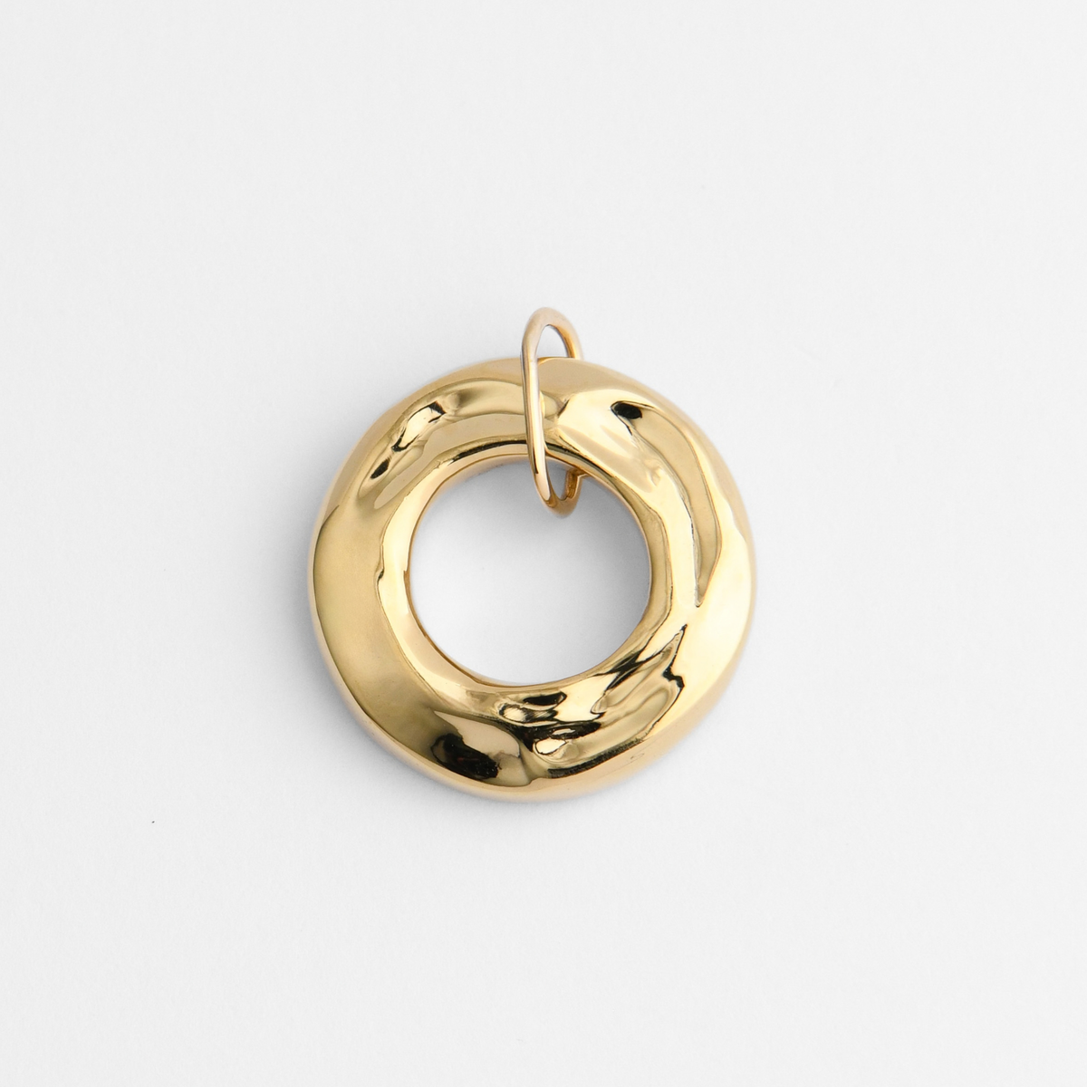 Dromi, a thick, rounded ring pendant in warm, golden-yellow brass, with a smooth, softly irregular surface and a large circular opening at its centre.