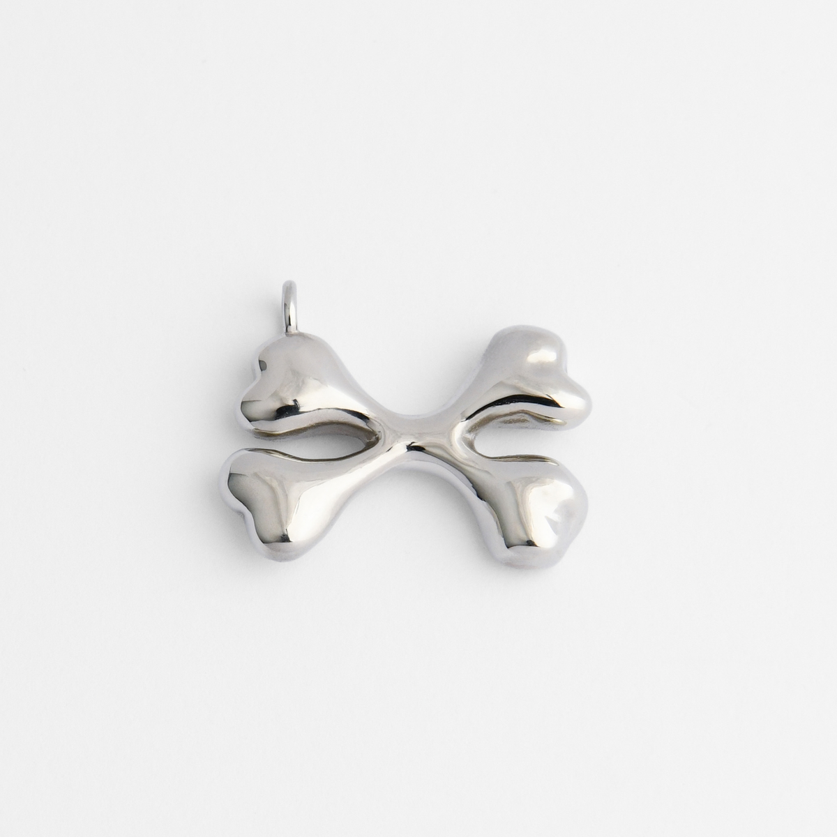 Bones, a pendant of two crossed bones in cool, silvery white bronze, with smooth, rounded forms and broad, softly sculpted ends.