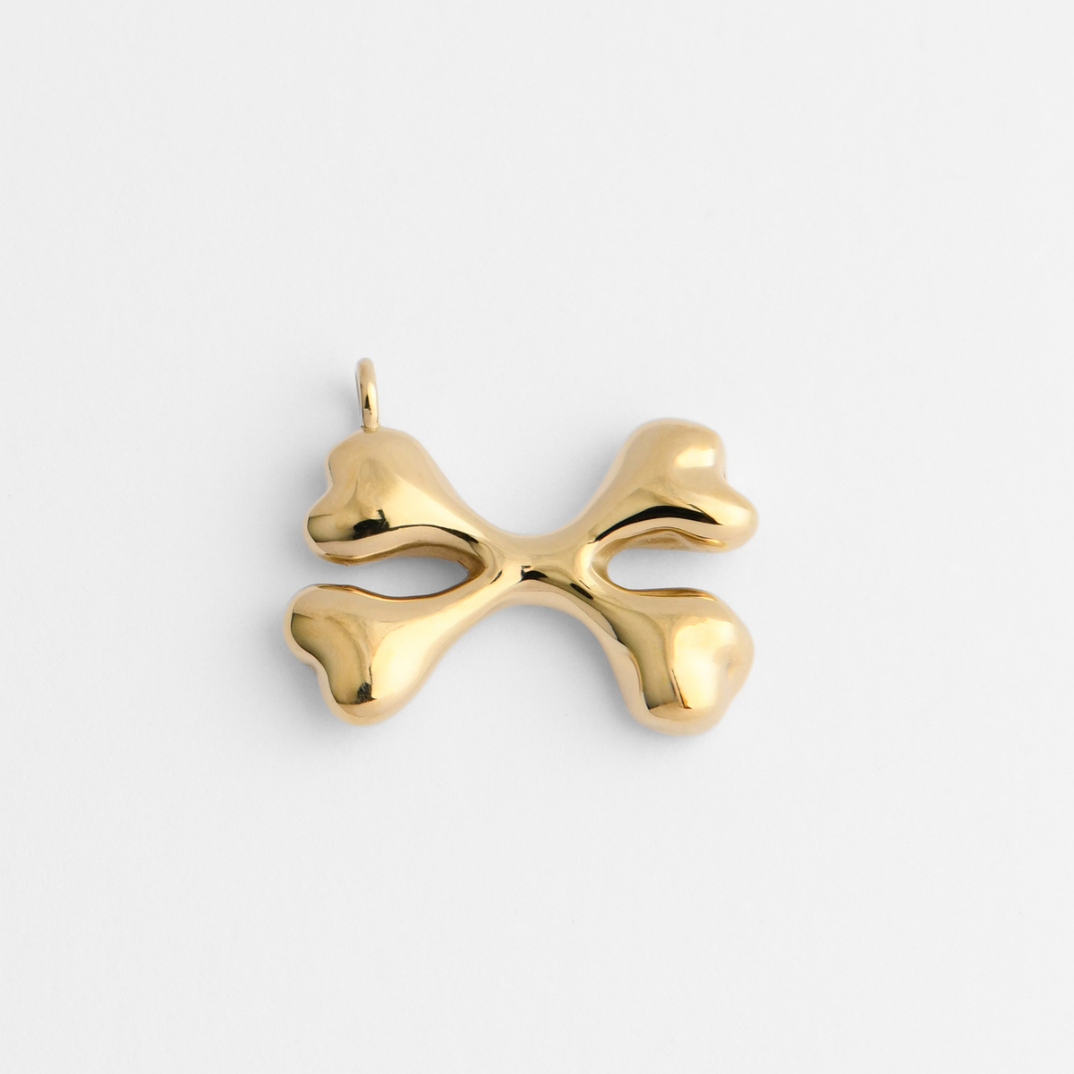 Bones, a pendant of two crossed bones in warm, golden-yellow brass, with smooth, rounded forms and broad, softly sculpted ends.