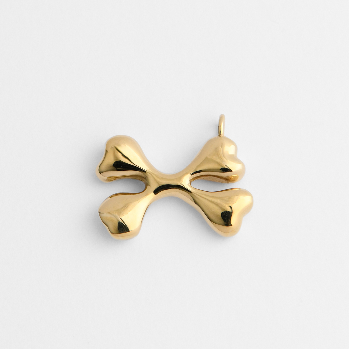 Bones, a pendant of two crossed bones in warm, golden-yellow brass, with smooth, rounded forms and broad, softly sculpted ends.
