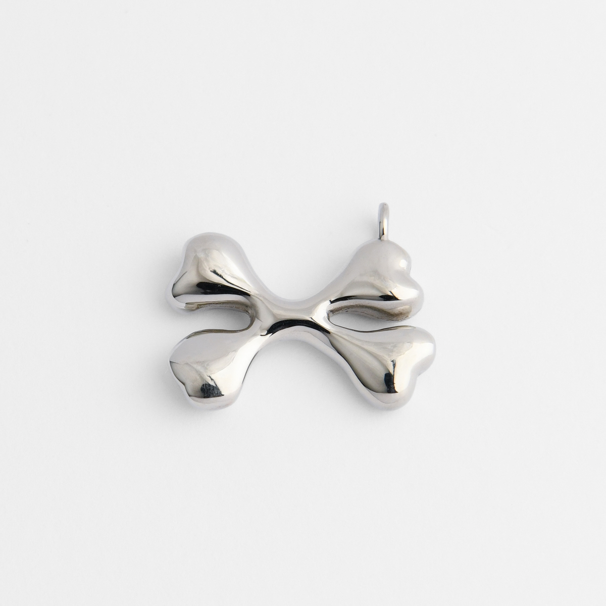 Bones, a pendant of two crossed bones in cool, silvery white bronze, with smooth, rounded forms and broad, softly sculpted ends.