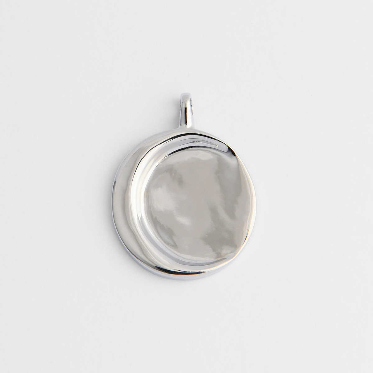 Caligo, a smooth round pendant in cool, silvery white bronze, with a raised crescent-shaped ridge sweeping around one side.
