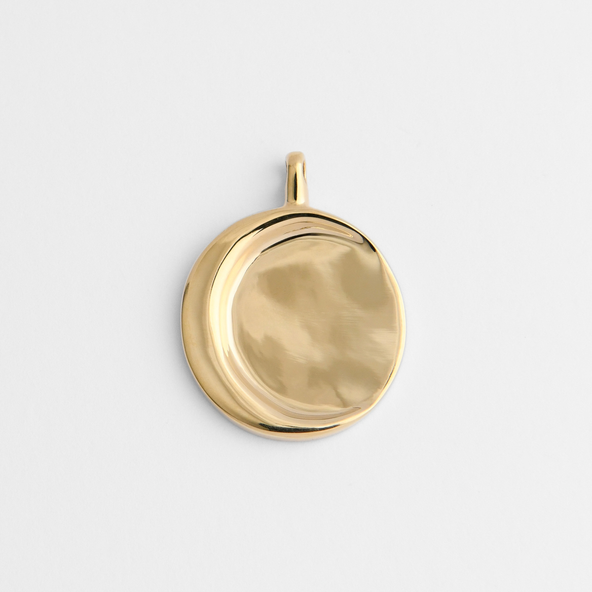 Caligo, a smooth round pendant in warm, golden-yellow brass, with a raised crescent-shaped ridge sweeping around the left side.