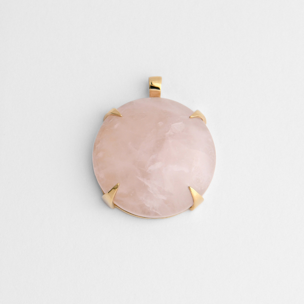 Spar, a round pendant in warm, golden-yellow brass, with four triangular claws holding pale pink rose quartz, softly translucent with natural variations in tone. As a natural stone, each piece varies.