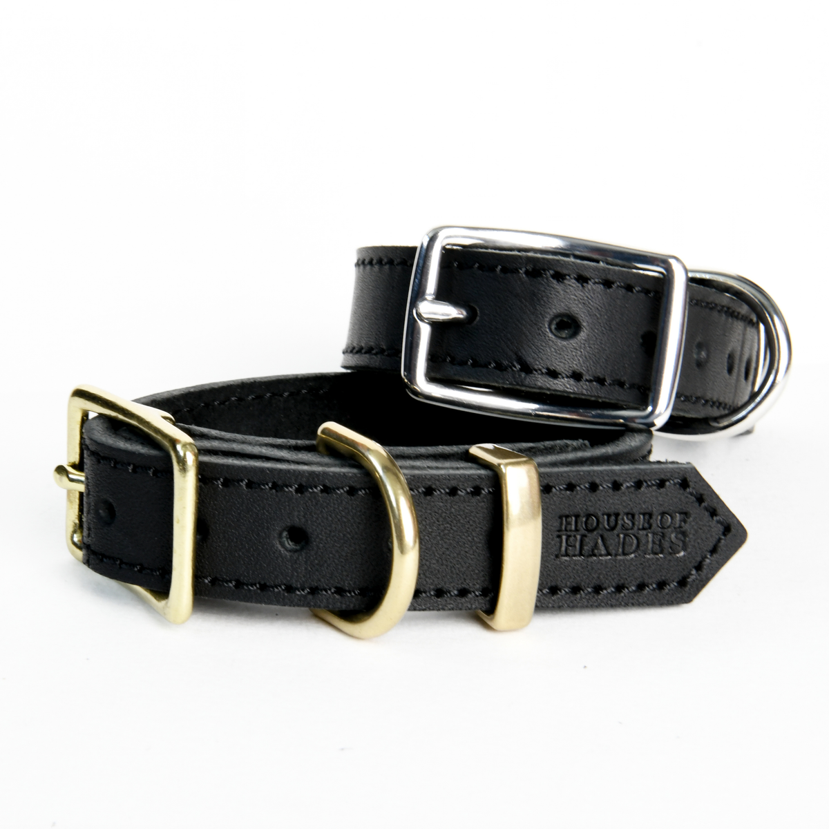 Two fastened black cowhide leather dog collars stacked together, the bottom collar has warm brass hardware and the other cool silver-colour hardware. Both feature a rectangular buckle, D-ring, keeper, black stitching across the smooth leather and House of Hades stamp with a pointed triangular end. 