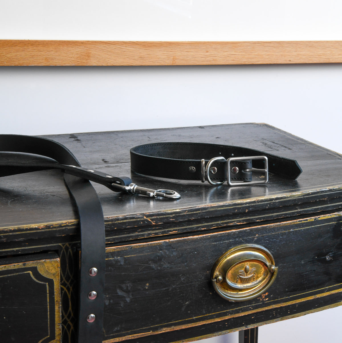 House of Hades black leather dog collar with silver-coloured buckle and matching leather lead with silver clasp, arranged across a weathered black antique wooden chest with brass detailing.