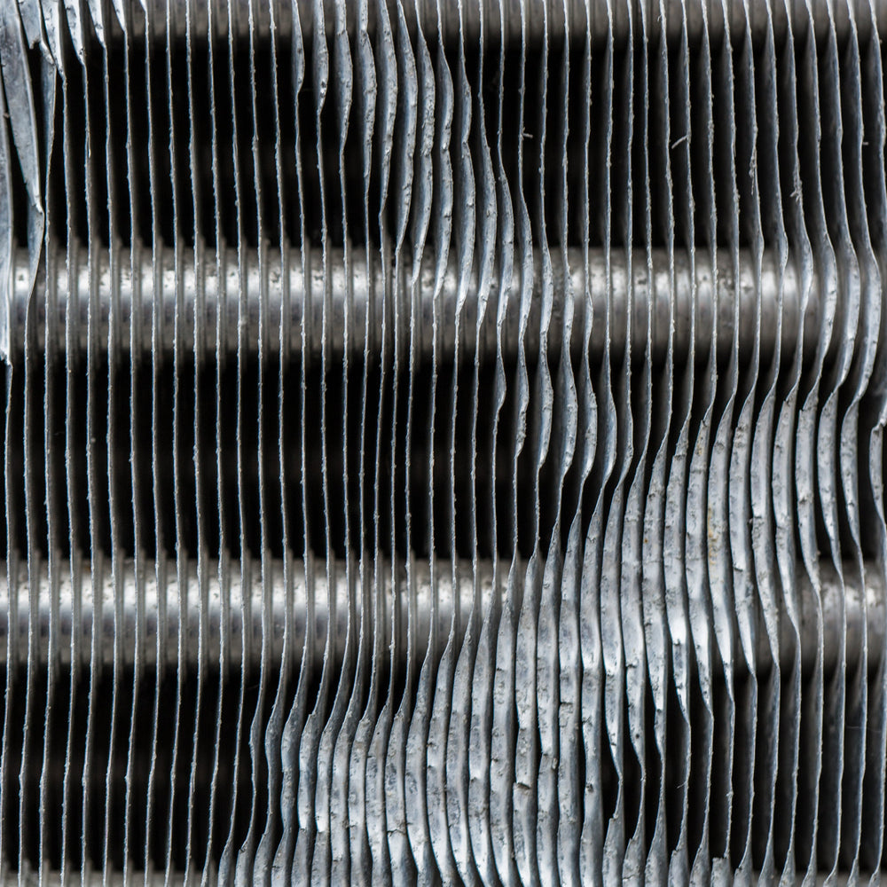 A close-cropped study of weathered silver metal, its repeating ridges catching bright light before disappearing into deep black shadow.